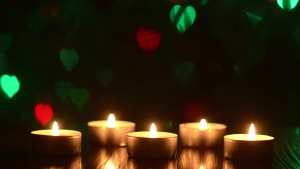 Brandende kaarsen op een tafel in een donkere kamer, feestelijke decoratie van de ruimte, kleurrijke bokeh hart knippert blauw rood groen. — Stockvideo