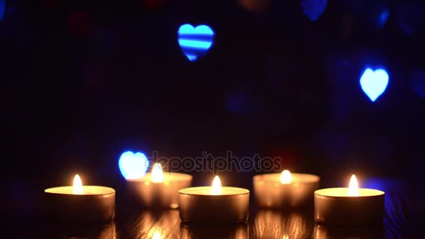 Κεριά καύση σε ένα τραπέζι σε ένα σκοτεινό δωμάτιο, διακόσμηση φωτός διακοπών, αναβοσβήνουν πολύχρωμα bokeh καρδιά μπλε κόκκινο πράσινο. — Αρχείο Βίντεο
