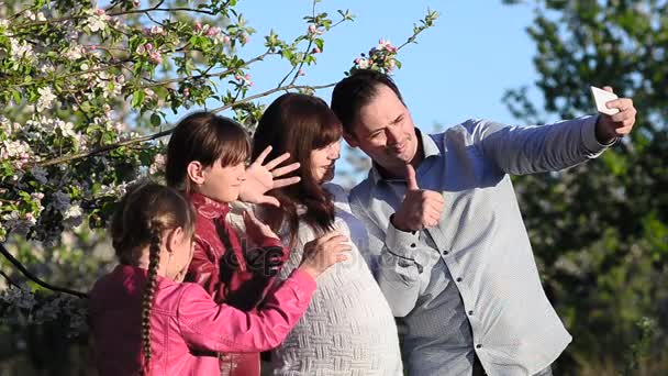 Maman enceinte, papa et fille prenant des photos de moi avec téléphone au printemps fleuri Parc, mère et enfants regardant des photos sur l'écran tactile dans le smartphone — Video