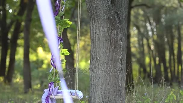 Swing på trädet dekorerade med blommor, blå band med röda blommor, vinden skakar vackra swing — Stockvideo