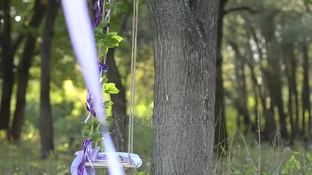 Swing op boom versierd met bloemen, blauw lint met rode bloemen, wind schudt mooie schommel — Stockvideo