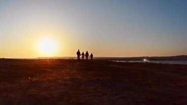 Mutlu bir aile Coast Körfezi üzerinde yürüme. Deniz kıyısında yürüyen bir aile. Siluetleri günbatımı.