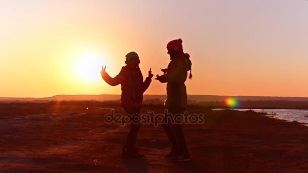 Ragazze con le cuffie che ballano sulla musica, ragazze con il telefono che ascoltano musica sulle cuffie contro il tramonto . — Video Stock