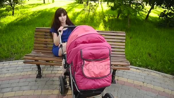 Bela jovem mãe andando com uma carruagem de bebê no parque . — Vídeo de Stock