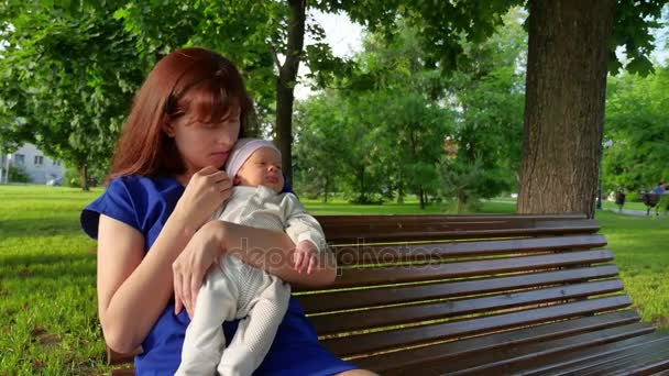 Мать сидит с ребенком на скамейке в парке, мать держит ребенка за руку — стоковое видео