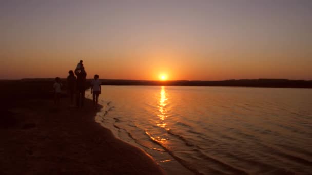 Familia camina a lo largo de la orilla al atardecer sol rojo. Movimiento lento . — Vídeos de Stock