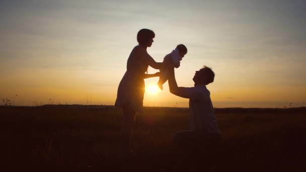 Mãe dá bebê para seu pai em braços contra o belo pôr do sol — Vídeo de Stock