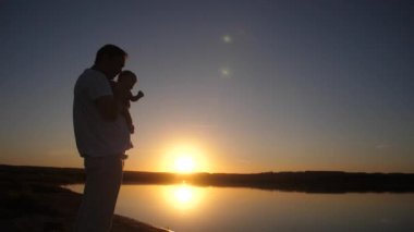 Adam bebek parmağını kırmızı güneş batımında mesafe gösterir. Ağır çekim.
