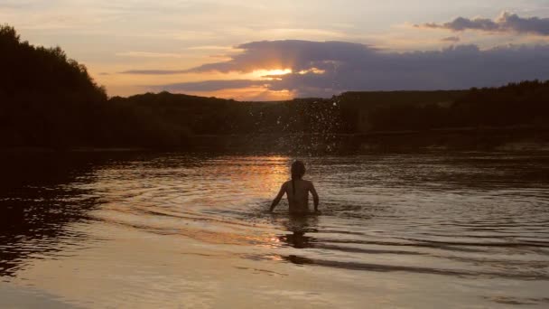 Девушка на закате играет в воде, девушка руки брызгает водой, медленное движение — стоковое видео