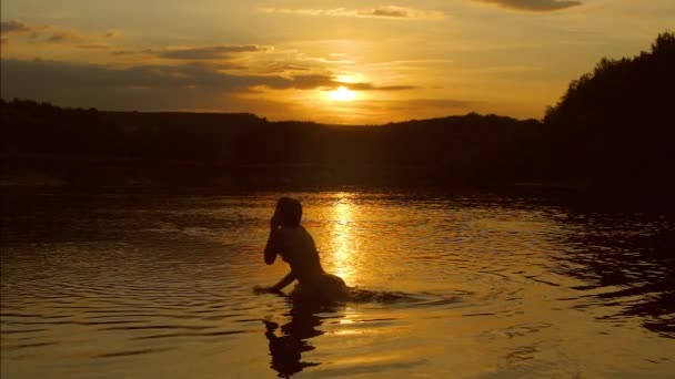 Chica joven saltando al agua sobre un fondo de puesta de sol, disparo en cámara lenta — Vídeo de stock