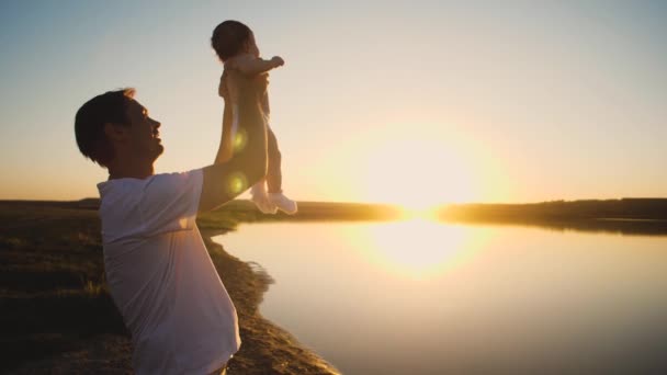 O pai tem um bebé pequeno nos braços ao pôr-do-sol da noite. Movimento lento . — Vídeo de Stock