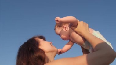 Anne Kucağında bebekle oynuyor ve mavi gökyüzü arka planı, ağır çekim sarılarak