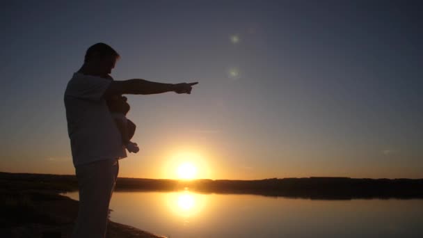 男は、赤い太陽の日没時の距離で赤ちゃんの指を示しています。スローモーション. — ストック動画