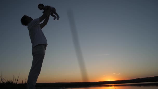 Padre cría a un pequeño bebé en brazos al atardecer del sol rojo de la noche. Movimiento lento . — Vídeo de stock