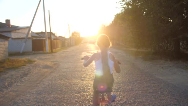 女の子は、夕日のまぶしさに、道路に沿って、自転車に乗っています。.スローモーション. — ストック動画