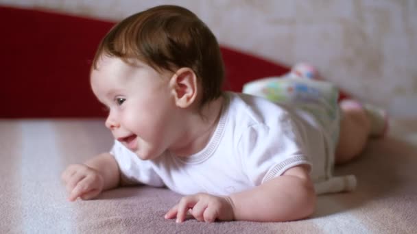 Baby liegt auf dem Bauch, blickt auf und lächelt. — Stockvideo