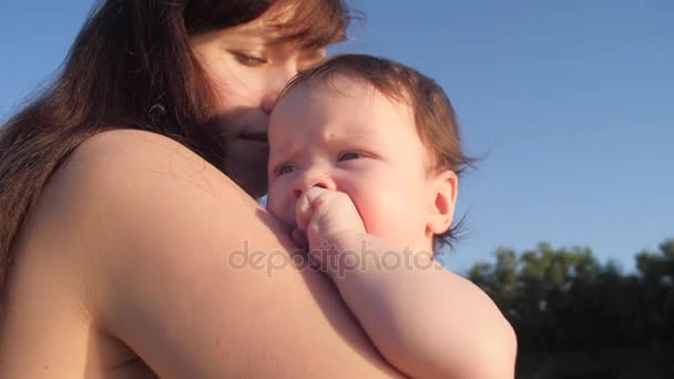 Mamá está sosteniendo al bebé en sus brazos contra el cielo azul, vacaciones familiares en la playa en verano — Vídeos de Stock