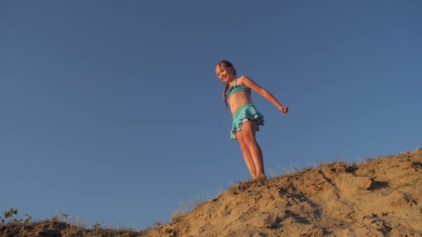 Malá šťastná dívka, která skočila na pláži proti modré obloze, pomalý pohyb snímání — Stock video