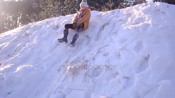 Щаслива дівчина-підліток котиться вниз по пагорбу зі снігом в зимовому парку на тлі засніжених лісів, морозний сонячний день у лісі . — стокове відео