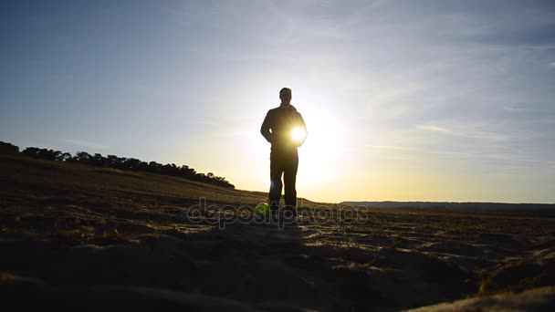 Silhuetten av mannen med bollen stående på stranden upplyst av solen. — Stockvideo