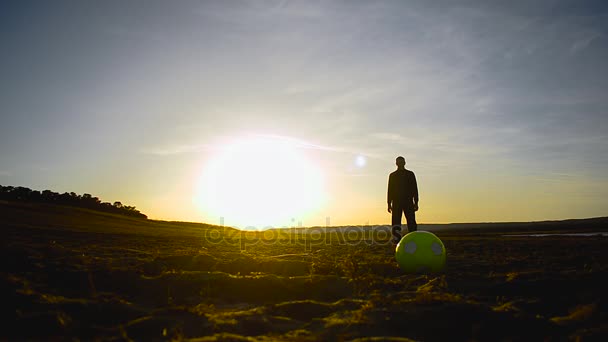 Silueta del hombre con la bola de pie en la playa iluminada por el sol . — Vídeo de stock