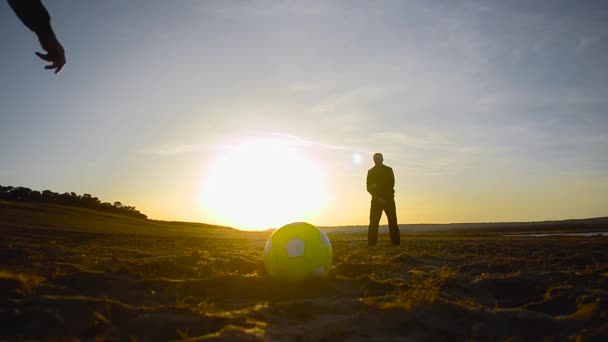 Patear una pelota de fútbol, portero atrapa pelota al atardecer, siluetas de los hombres jugando fútbol en la playa — Vídeo de stock