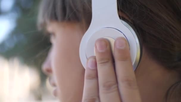 Alegre joven en auriculares escuchando música y bailando en el parque en verano, primer plano — Vídeo de stock