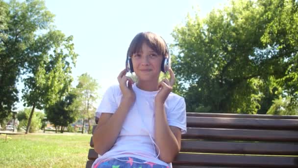 Красива молода дівчина з навушниками слухає музику і танцює в літньому парку — стокове відео