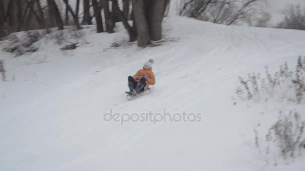 Счастливый ребенок зимой катается со снежной горки . — стоковое видео
