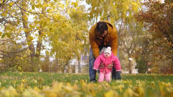 Baby with his father jumping their feet on green grass in fall and smiling. Slow motion. — Stock Video