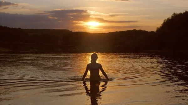 Jong meisje komt uit het water op zonsondergang achtergrond, Slow motion — Stockfoto