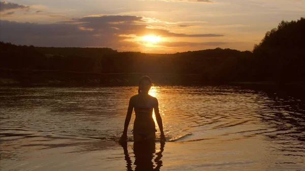 Молодая девушка выходит из воды на фоне заката, медленное движение — стоковое фото