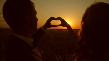 Silhouette kız ve erkek arkadaşı kalp şekli güzel gün batımını karşı kendi elleriyle yapar.