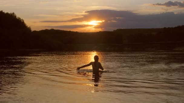 Jovem dança na água e olha para o pôr do sol, câmera lenta — Vídeo de Stock