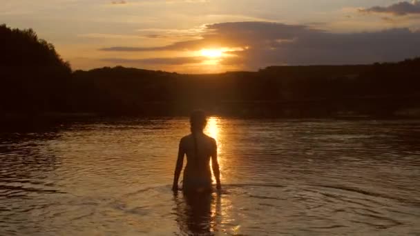 Adolescente vai para a água ao pôr do sol . — Vídeo de Stock