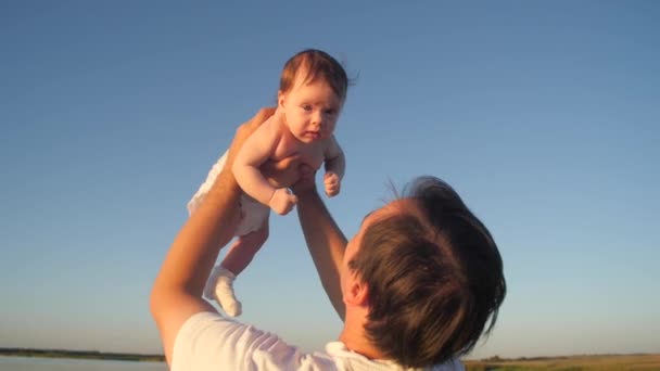 Padre sostiene al bebé en sus brazos y besos en la mejilla, contra el fondo del cielo azul . — Vídeos de Stock