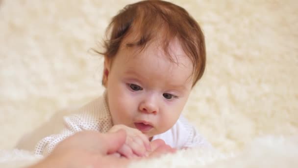 Papá juega con el bebé hermoso, niño pequeño se acuesta en el sofá y mira a los papás de la mano, de cerca — Vídeo de stock