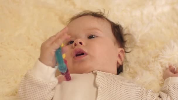 体内の赤ちゃんベビーベッドで仰向けし、彼の手でおもちゃを保持. — ストック動画
