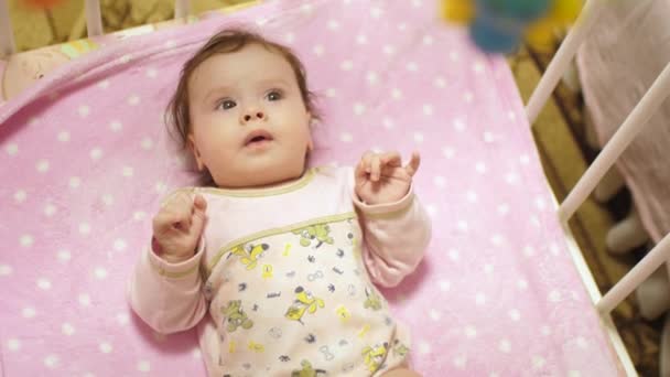 Baby i kroppen ligger på rygg i spjälsängen och ser på leksaker. Slow motion — Stockvideo