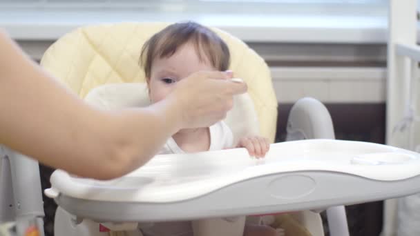 Το παιδί τρώει χυλό από κουτάλι κάθεται σε καρεκλάκι στην κουζίνα. — Αρχείο Βίντεο