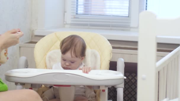 Ребенок ест кашу с ложки сидя на стульчике на кухне . — стоковое видео