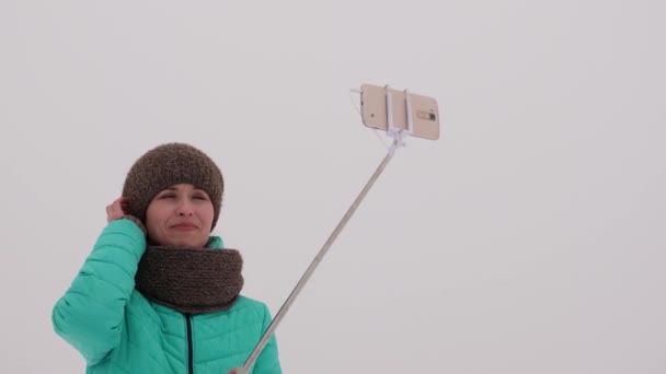 Kız telefon sopa sopa ile poz ve kışın, kar park gülümseyen. — Stok video