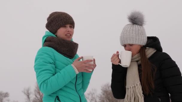 Meninas congeladas no frio falando e bebendo bebidas quentes de óculos ri sorrindo . — Vídeo de Stock