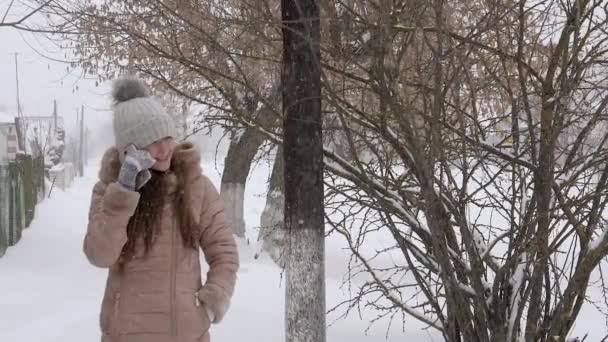 Glad tjej prata telefon promenader på snötäckta staden och leende. Snöstorm. Slow Motion. — Stockvideo
