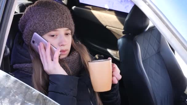 Ung vacker flicka sitter framför sätet i bilen och prata på telefon, dricka kaffe och leende. — Stockvideo