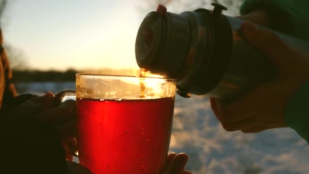 As pessoas derramam uma bebida quente de uma garrafa térmica em um copo ao pôr do sol brilhante . — Vídeo de Stock