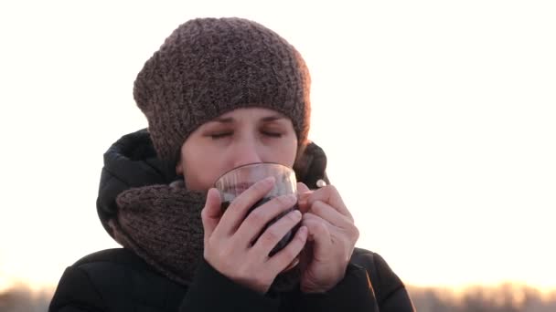 女人用一杯热茶和微笑来温暖你。在空旷的寒冷的空气中喝茶. — 图库视频影像