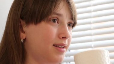 Güzel kız sıcak kahve pencere ve gülümsüyor tarafından oturan tadına sahiptir.