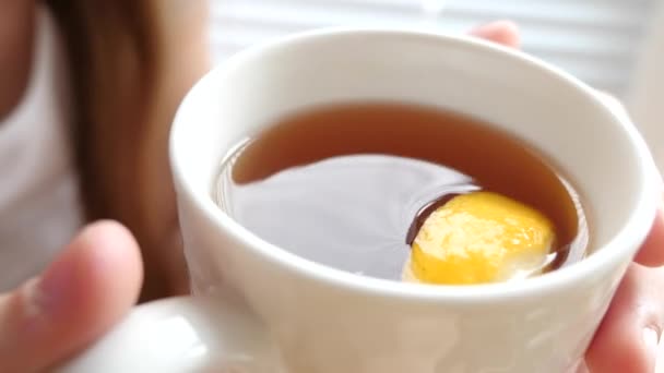 Thé d'or chaud avec tranche de citron, fille dans ses mains, qui se tient à la fenêtre . — Video