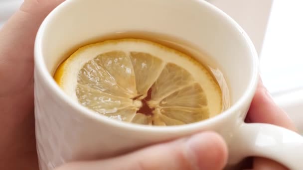 Hideg lány italok forró arany tea citrom álló ablak. — Stock videók
